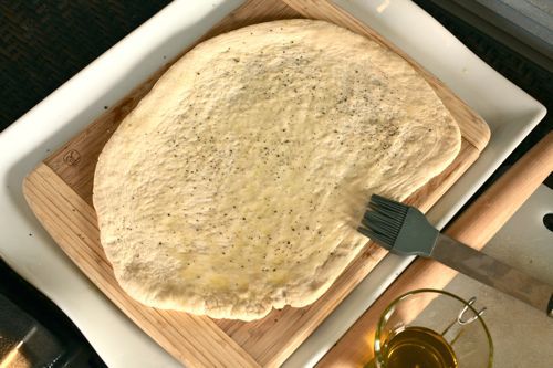 Brushing a rolled out piece of pizza dough with oil.