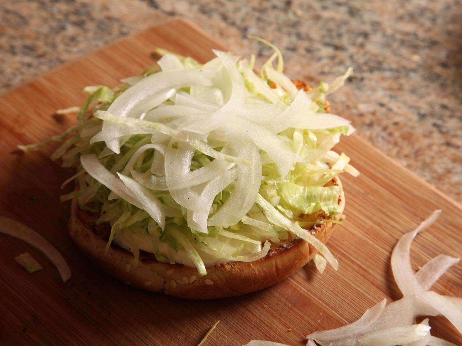 Shredded lettuce and sliced onion are placed atop the mayo-slathered bun.