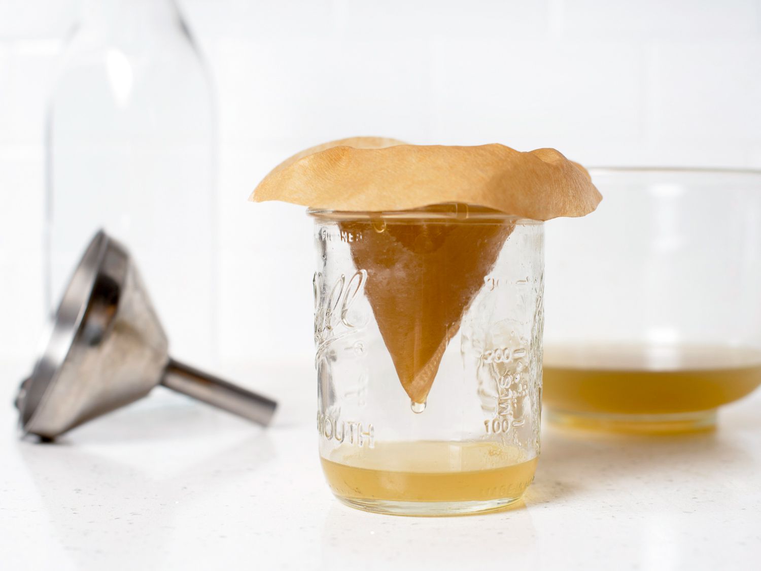Straining the combined liquids for falernum through a coffee filter into a glass jar.