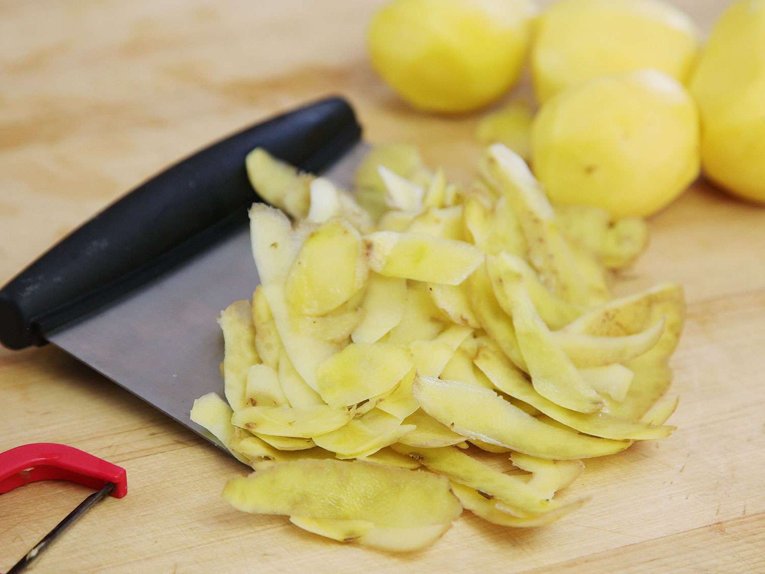 Pile of potato peels next to peeled potatoes.
