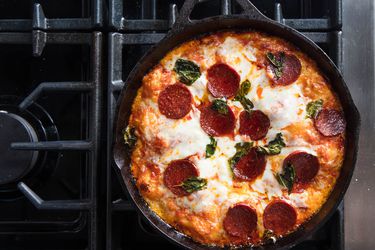 Overhead view of a pan pizza topped with pepperoni and torn basil leaves.