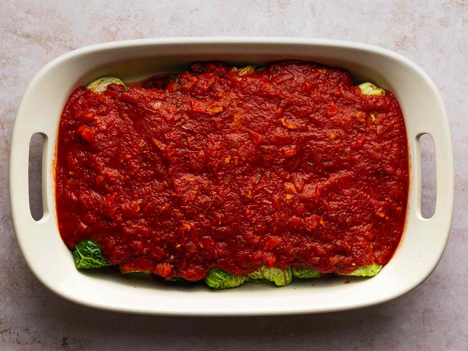 Cabbage rolls packed tightly in prepared 9- by 13-inch baking dish, with sauce poured on top.