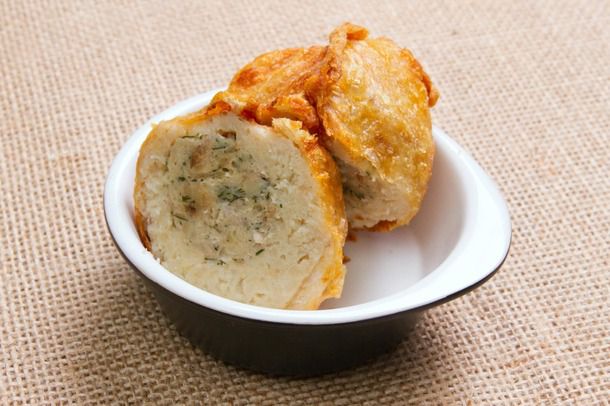 A small bowl holding two crispy deep-fried stuffed matzo ball halves, with the filling visible