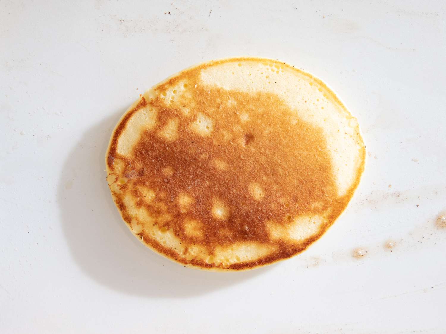 A single pancake shown from above on a white surface