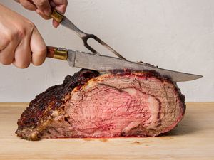 A cooked prime rib roast being carved with a knife and fork on a cutting board