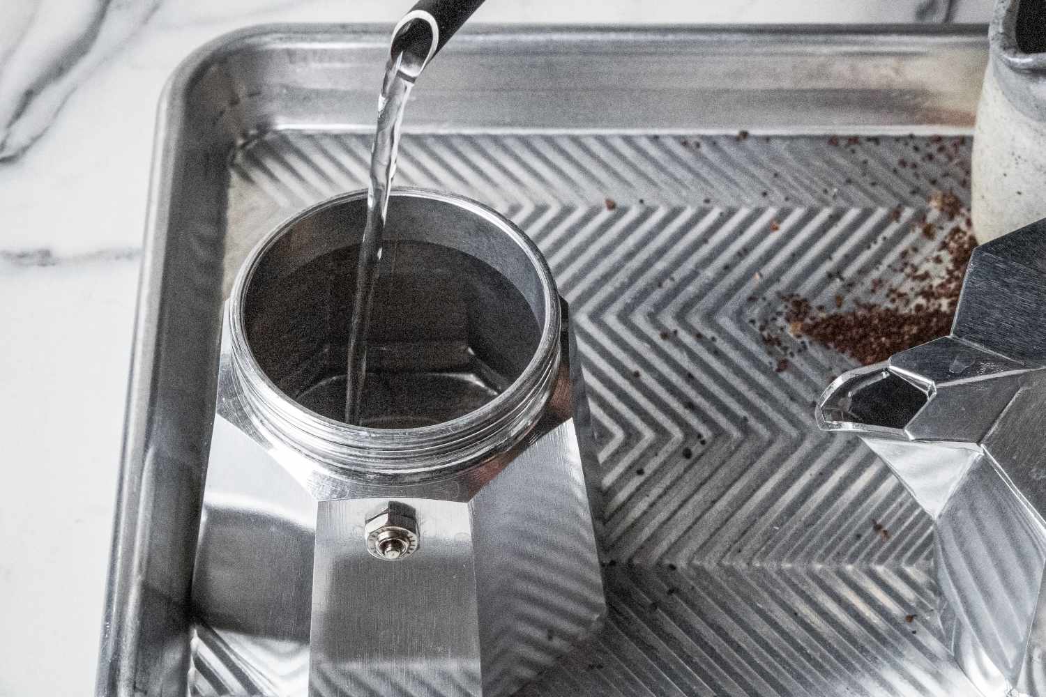 A person pouring water into the base of the Bialetti Moka Express moka pot.