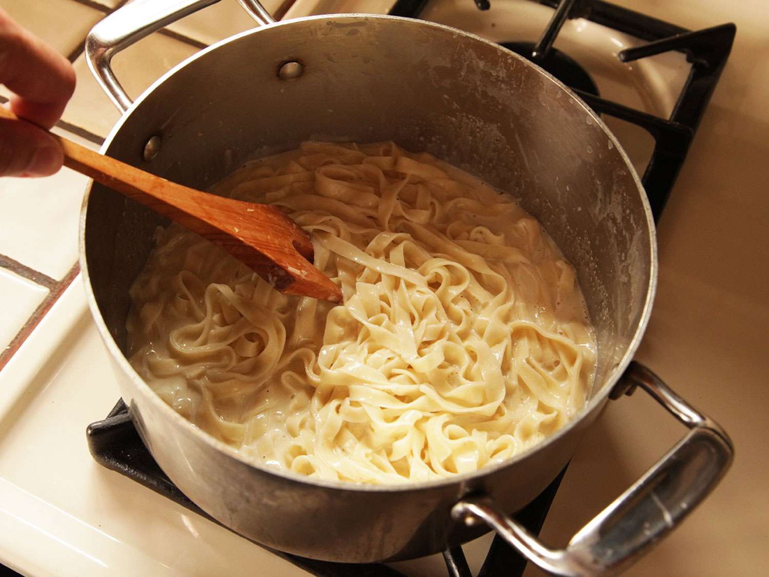 Stirring pasta into Alfredo sauce.