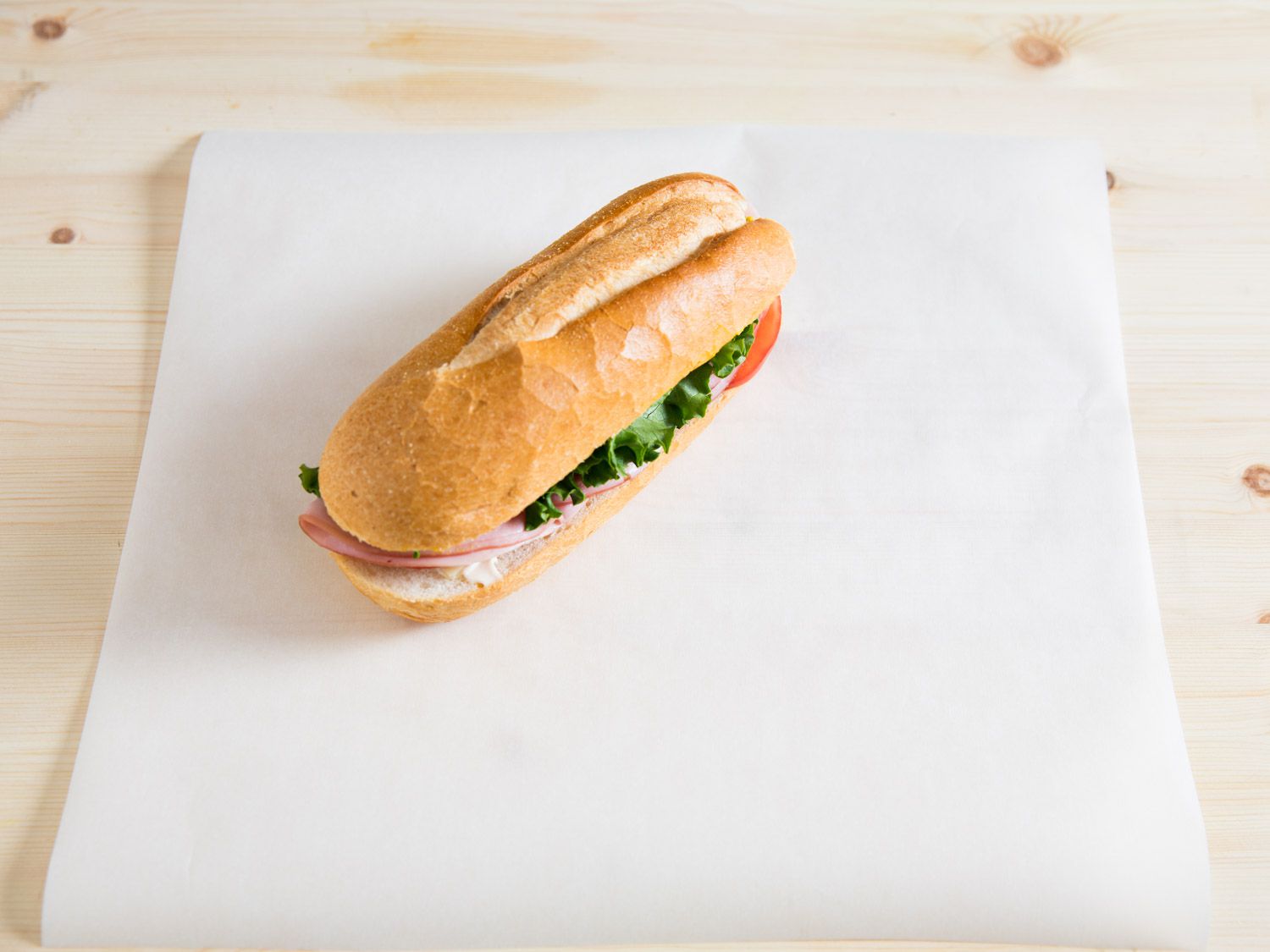 A sandwich on a long hero roll on top of a piece of paper.