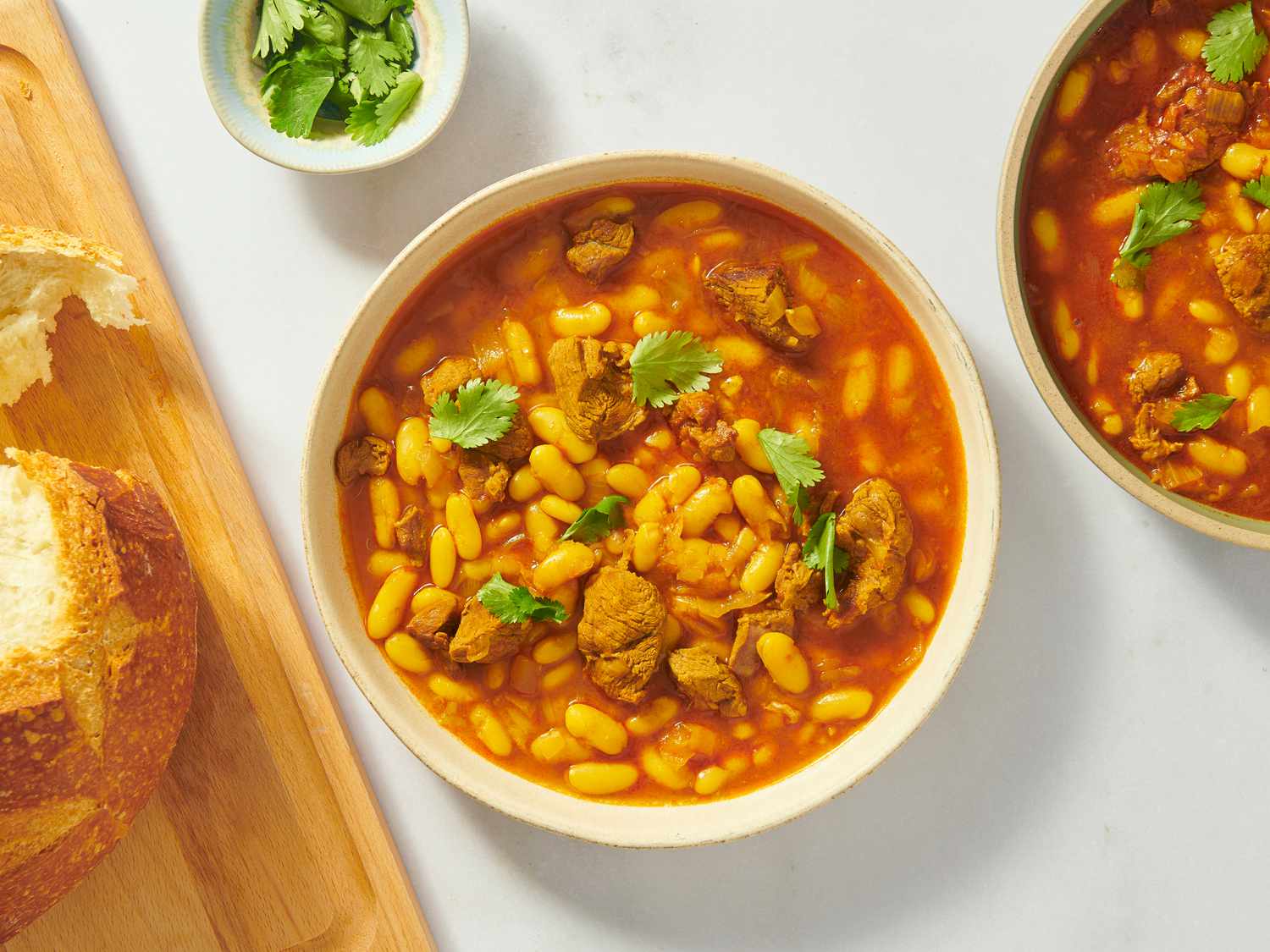 2 bowls of Moroccan white bean stew, with wooden board with bread on the left