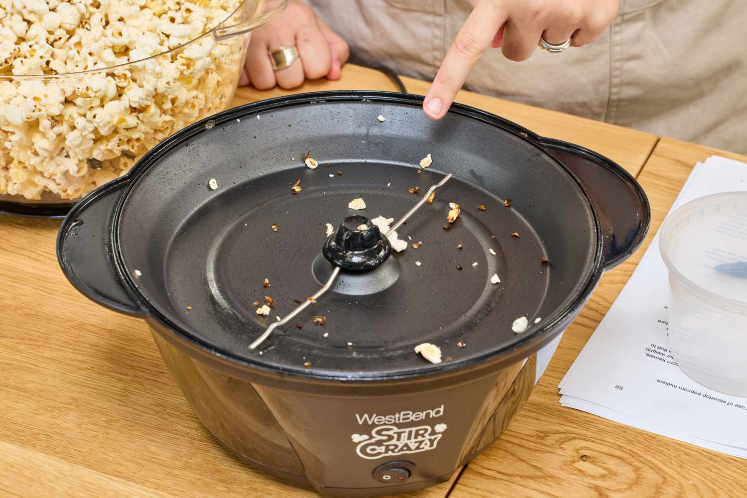 A person points to the bottom of the West Bend Stir Crazy Electric Hot Oil Popcorn Popper after use