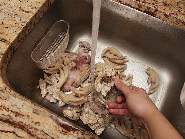Rinsing blanched chicken carcass and feet under running water.