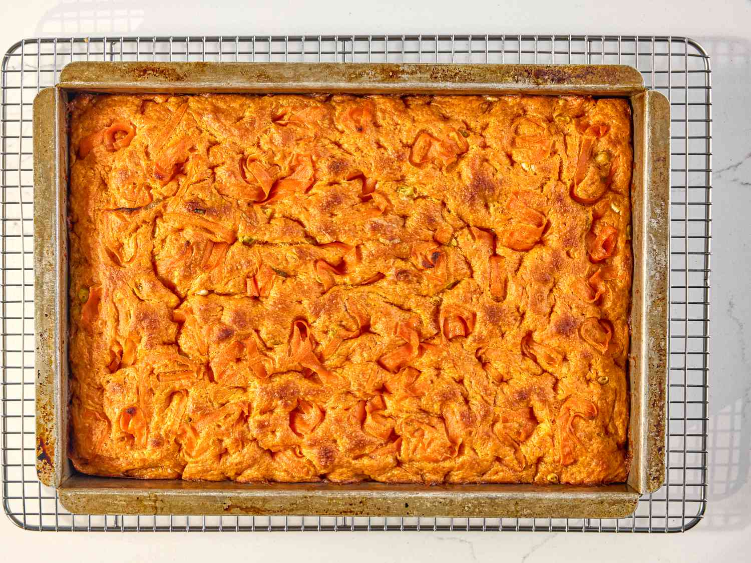 Rectangular carrot focaccia bread in a baking tray on a cooling rack