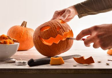 A person carving a jackolantern face on a pumpkin using a knife