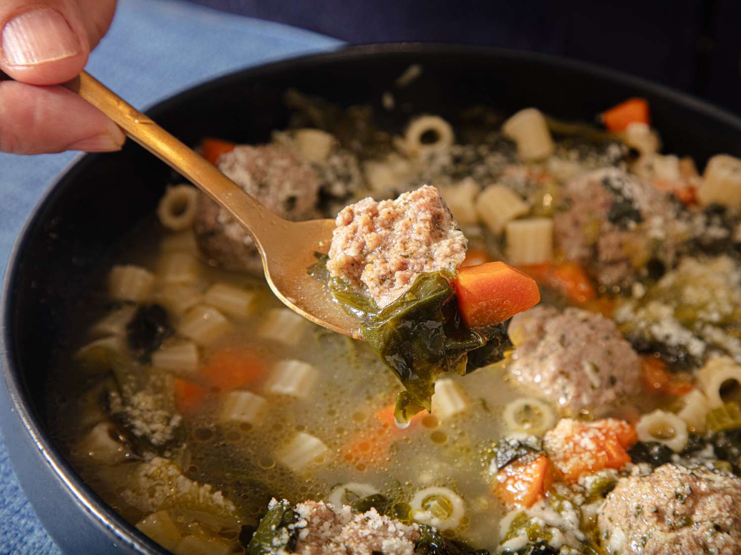 A spoon lifting a meatball and greens from a bowl of Italian wedding soup showing pasta carrots and broth