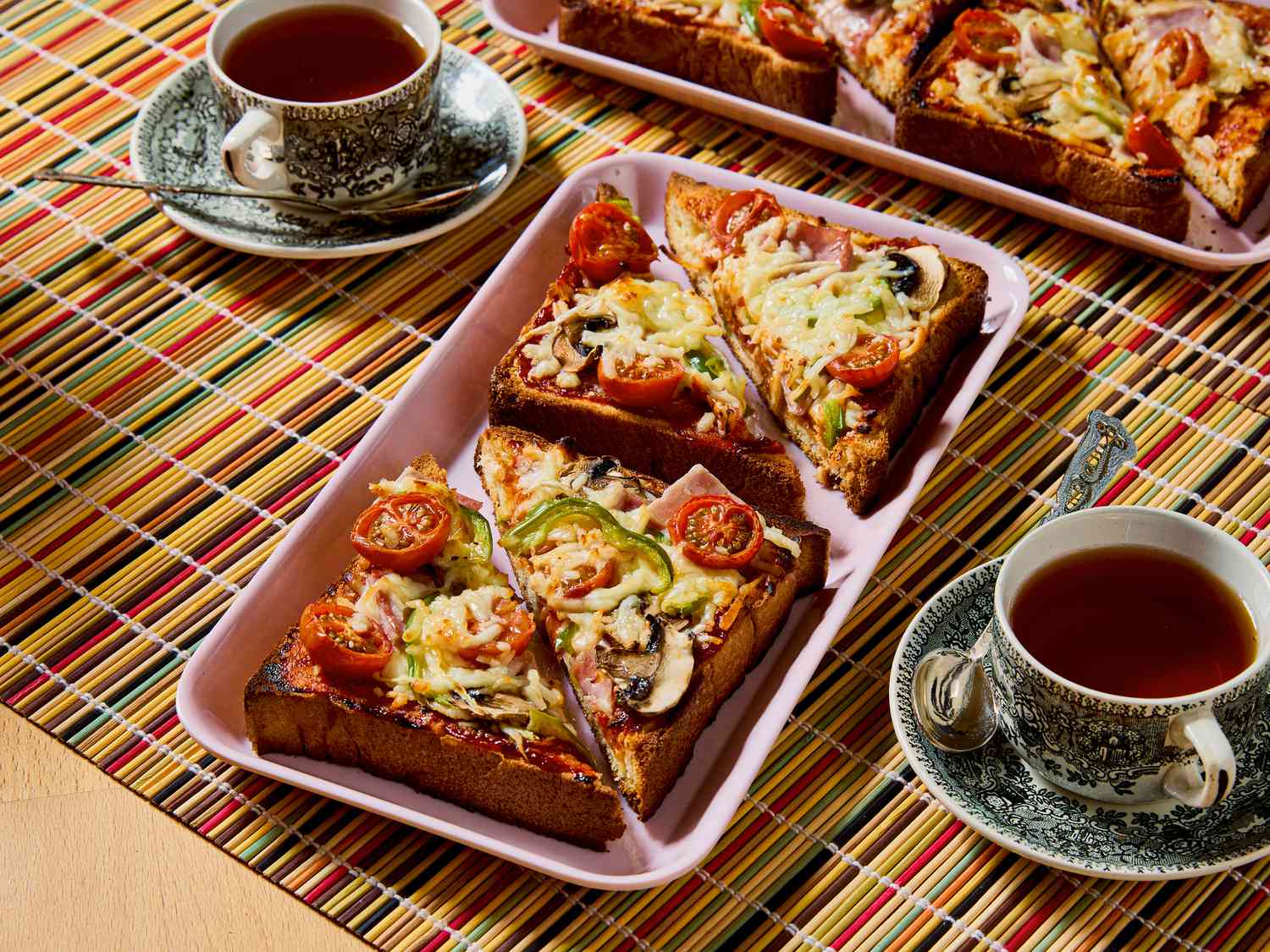 Slices of pizza toast arranged on a tray with cups of tea