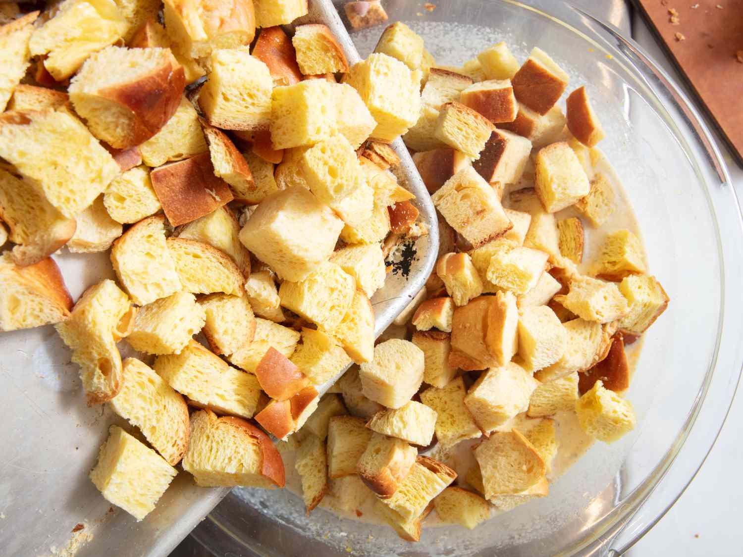 pouring tray of bread into glass bowl of mixtue