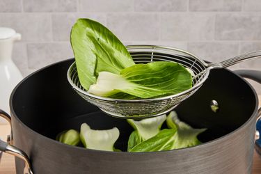 A metal spider strainer lifting bok chou from a stockpot