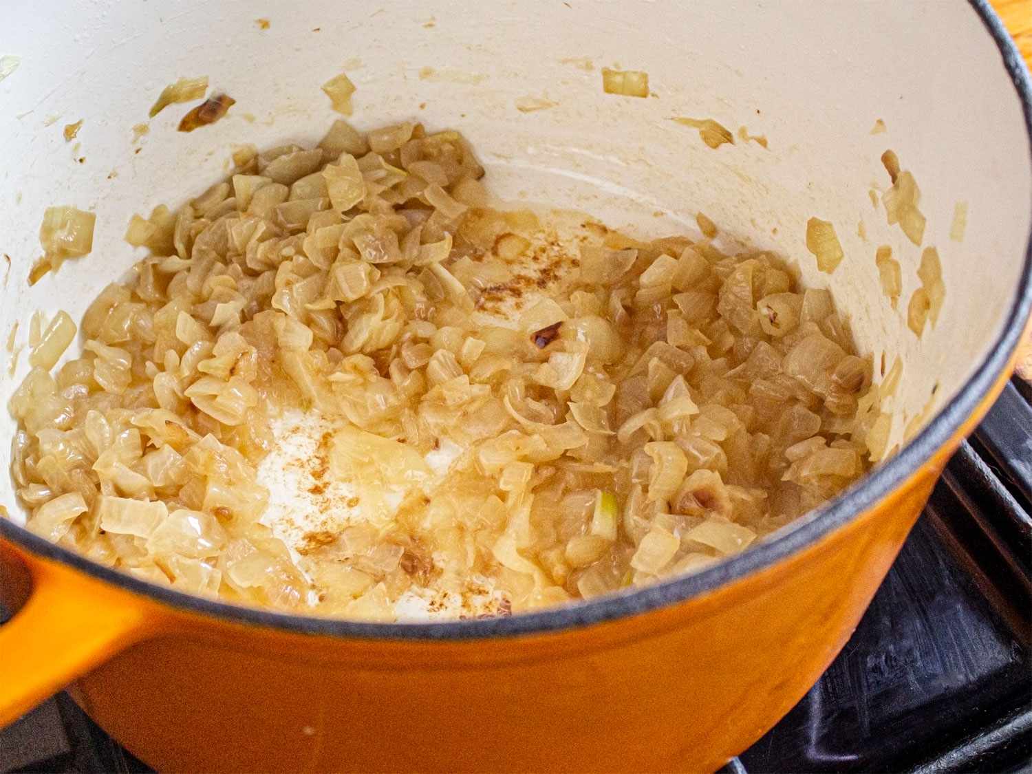 Side angle view of onions softened in an orange dutch oven on the stove