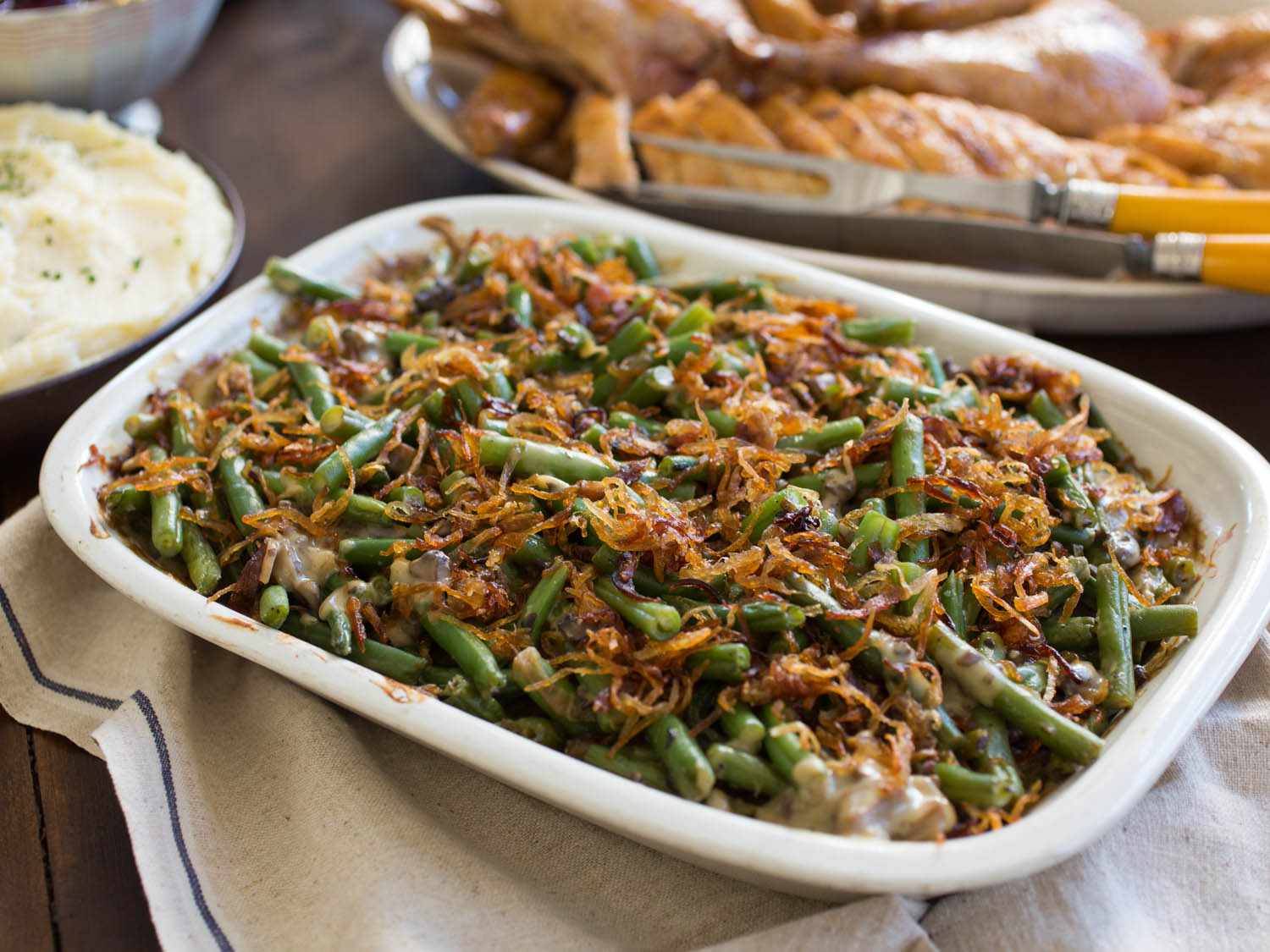 Green bean casserole, with mashed potatoes and carved turkey in the background.