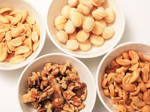 Four white bowls holding different types of nuts.