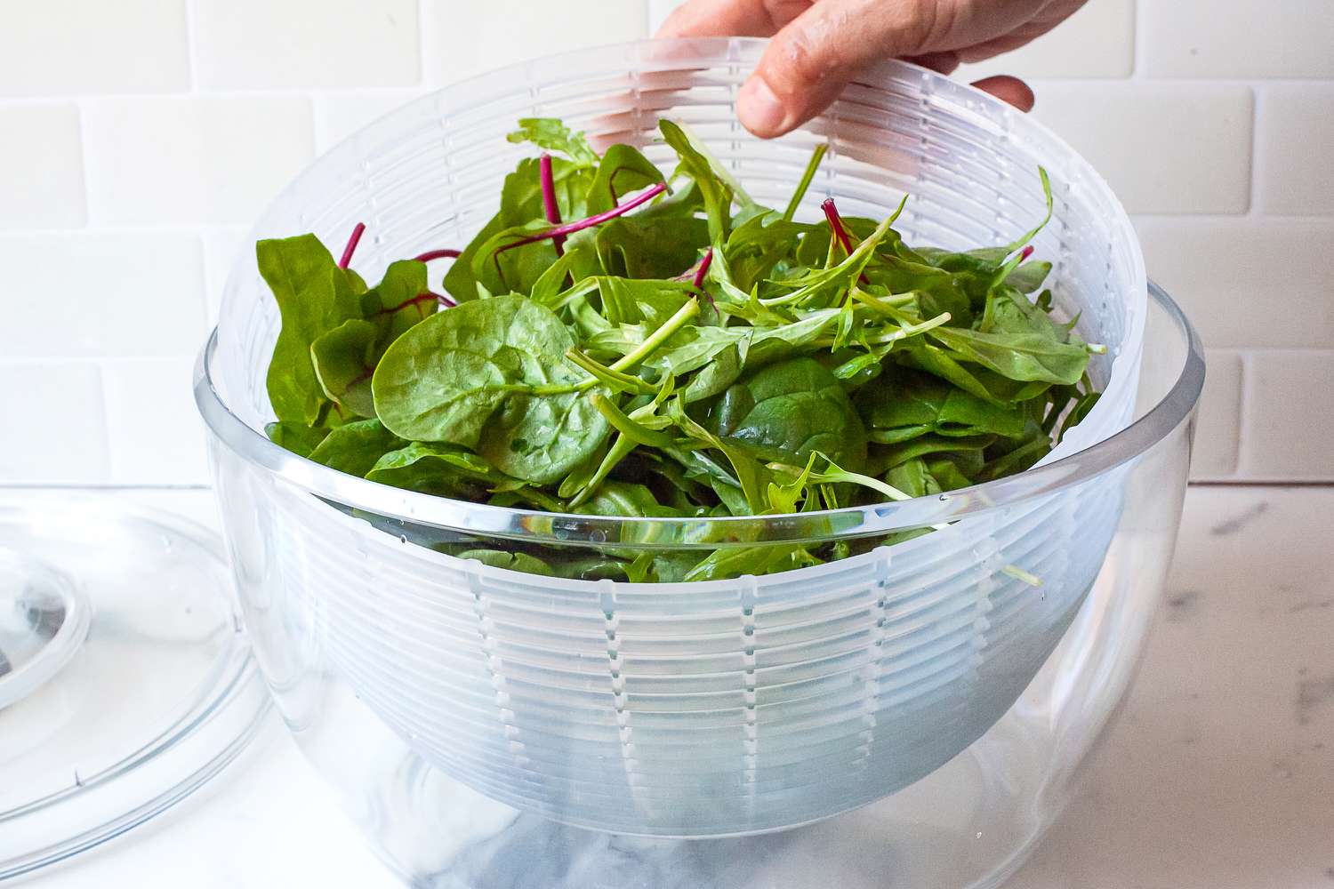 placing a bowl of greens in the plastic oxo spinner
