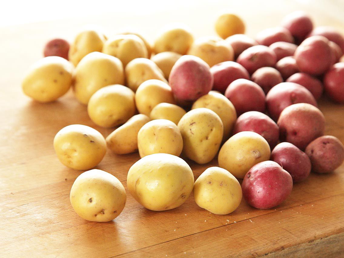 Red and white new potatoes on wooden cutting board.