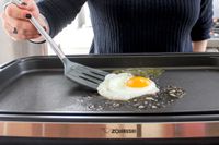A person using the Tovolo Silicone Slotted Turner to flip an egg