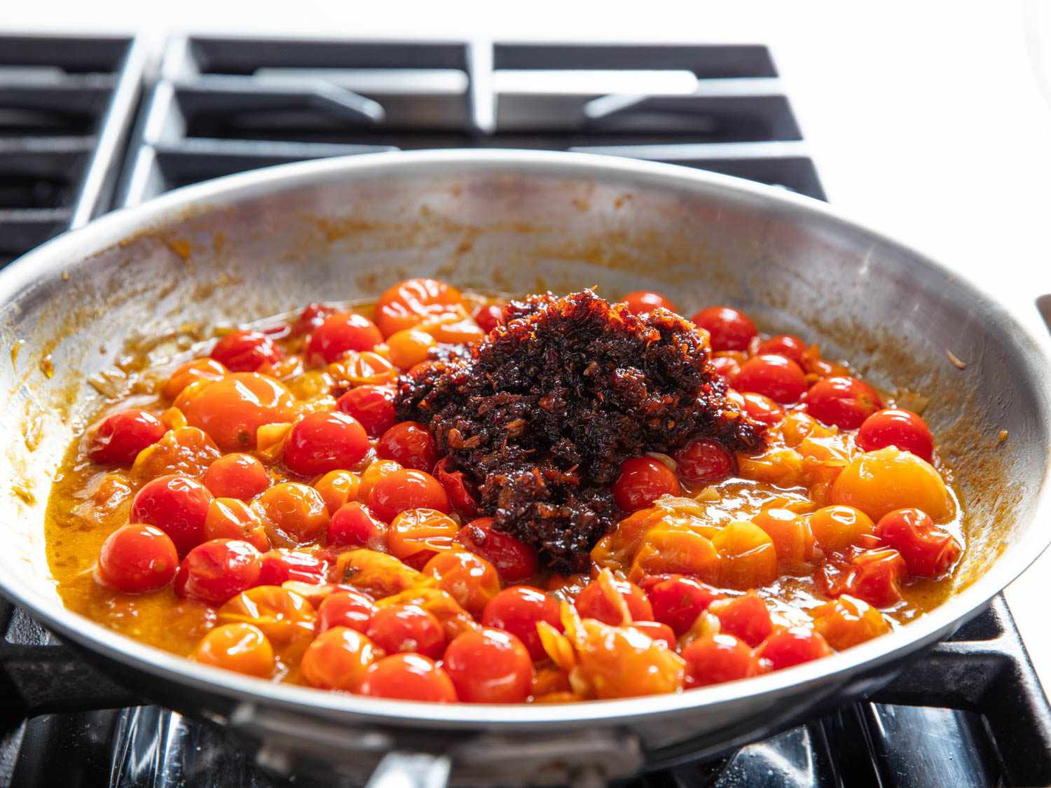Side view of a heaping amount of XO sauce that has just been added to skillet with burst cherry tomatoes.