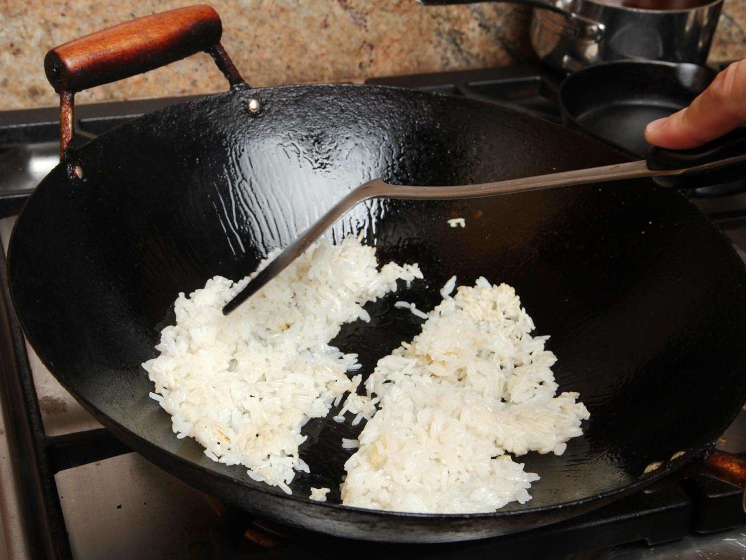 Cooked jasmine rice is broken up and fried in a wok.