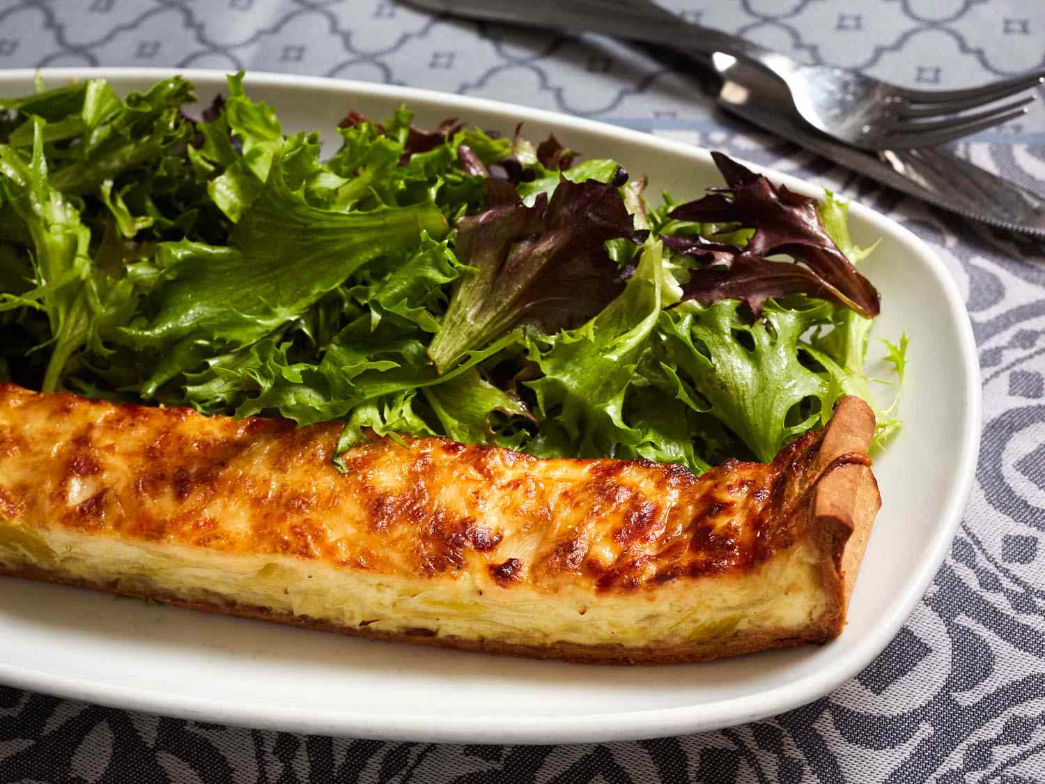 Convivial's uniquely shaped quiche (long and narrow) next to dressed greens.