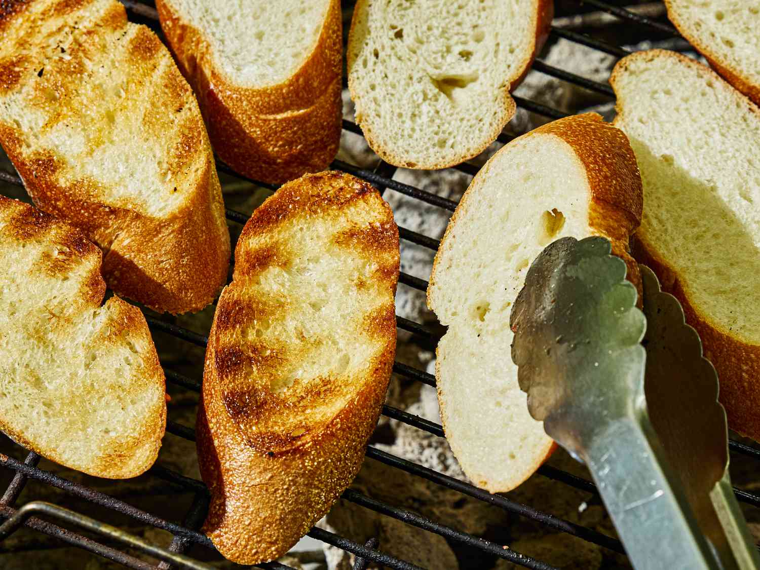 Slices of bread toasting on a grill with tongs visible nearby