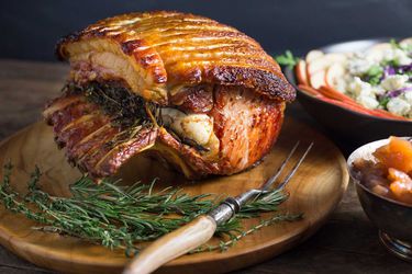 A whole roasted pork loin with golden crackling on a wooden platter
