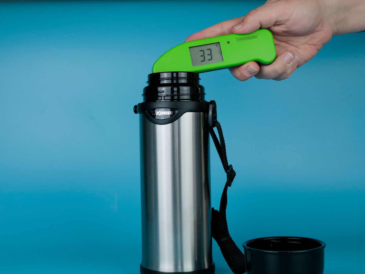 A person using a Thermapen to take the temperature of cold water inside of a thermos