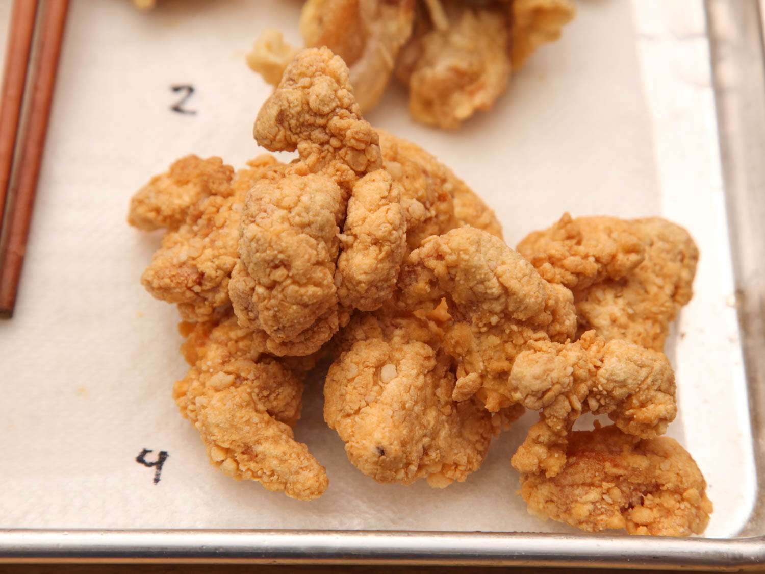 Double-breaded and fried chicken thighs on a paper towel-lined baking sheet.