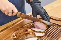 A person slices meat with the Miyabi Mizu SG2 9.5 Inch Slicing Knife