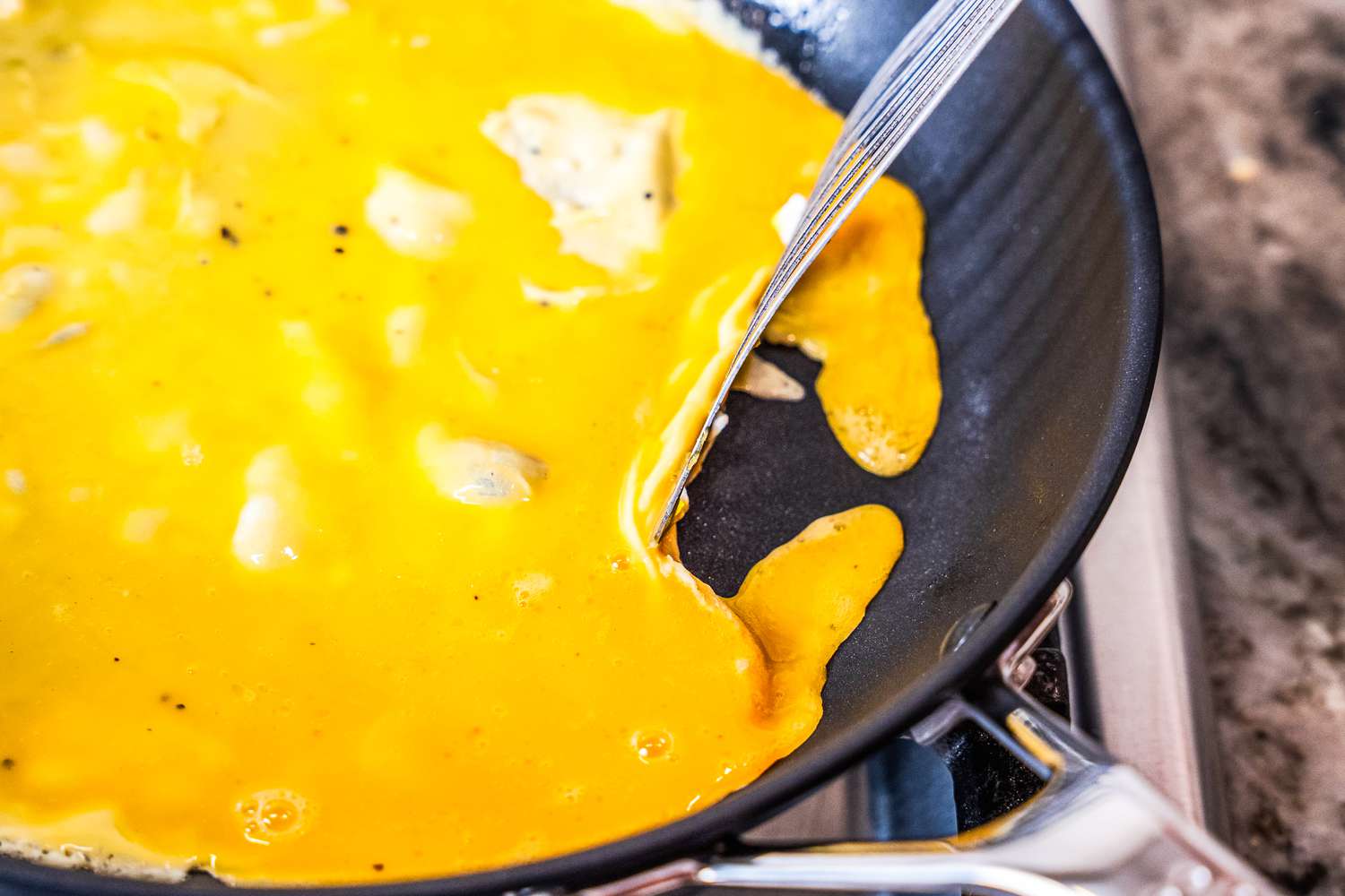 Scrambled eggs being cooked with a metal fish spatula in the Misen nonstick pan