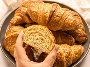 A plate of croissants with a hand holding a halved croissant showing its layers