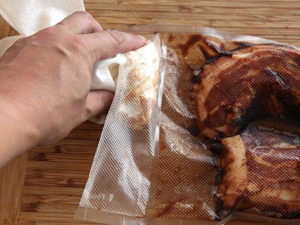 Wiping down the edges of a sous vide bag filled with pork belly