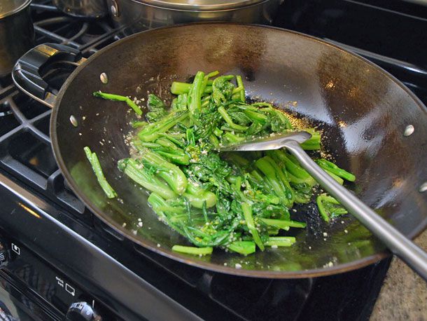 Tossing together cooked choy sum and sauce in a wok