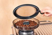 A person lifting up the lid of the coffee grinder section of the Breville Barista Touch Impress Espresso Machine with Grinder