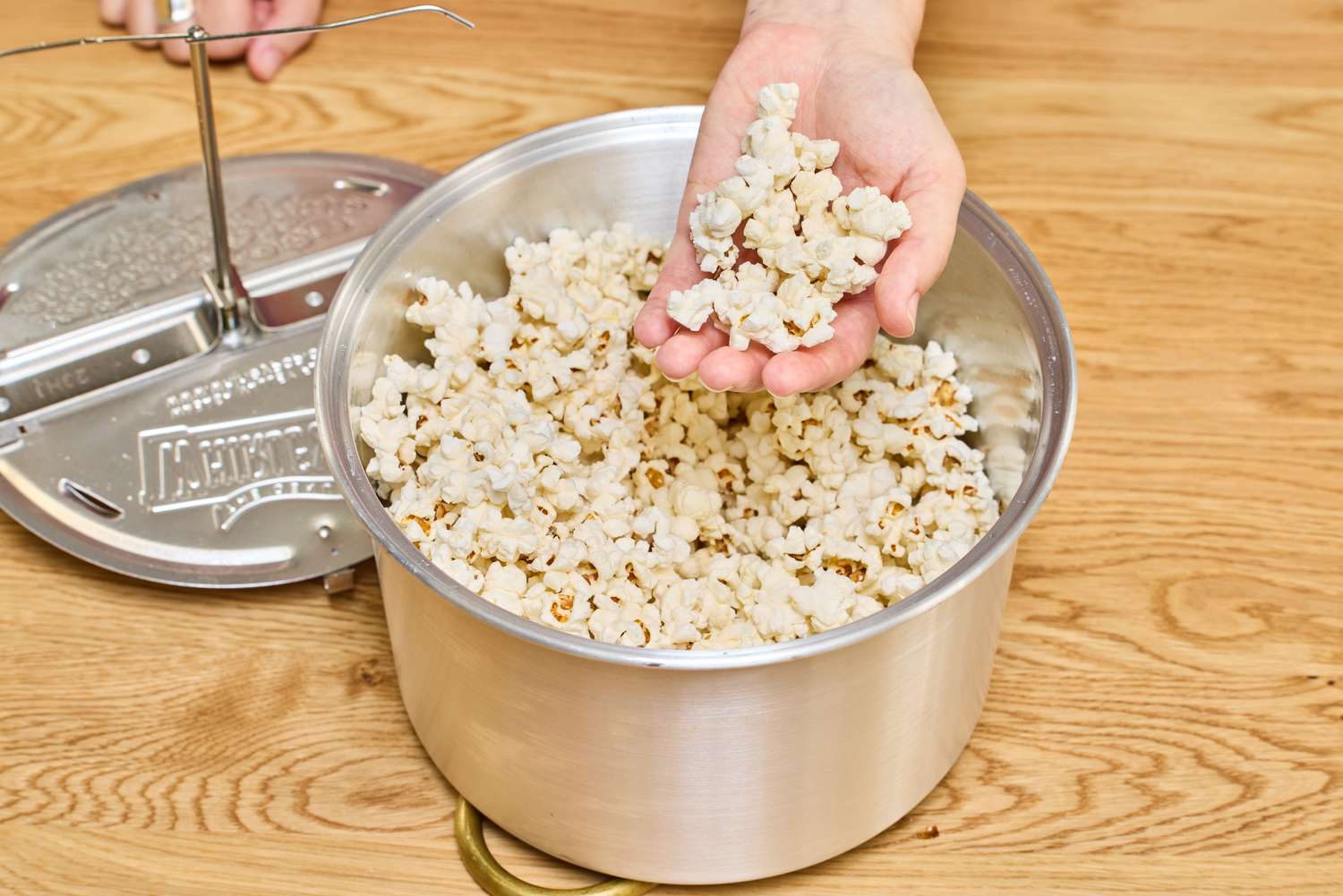 A person grabs a handful of popcorn from a Wabash Valley Farms Original Whirley Pop.