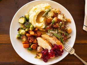 A Thanksgiving dinner plate consisting of mashed potatoes roasted vegetables stuffing turkey with cranberry sauce and a fork