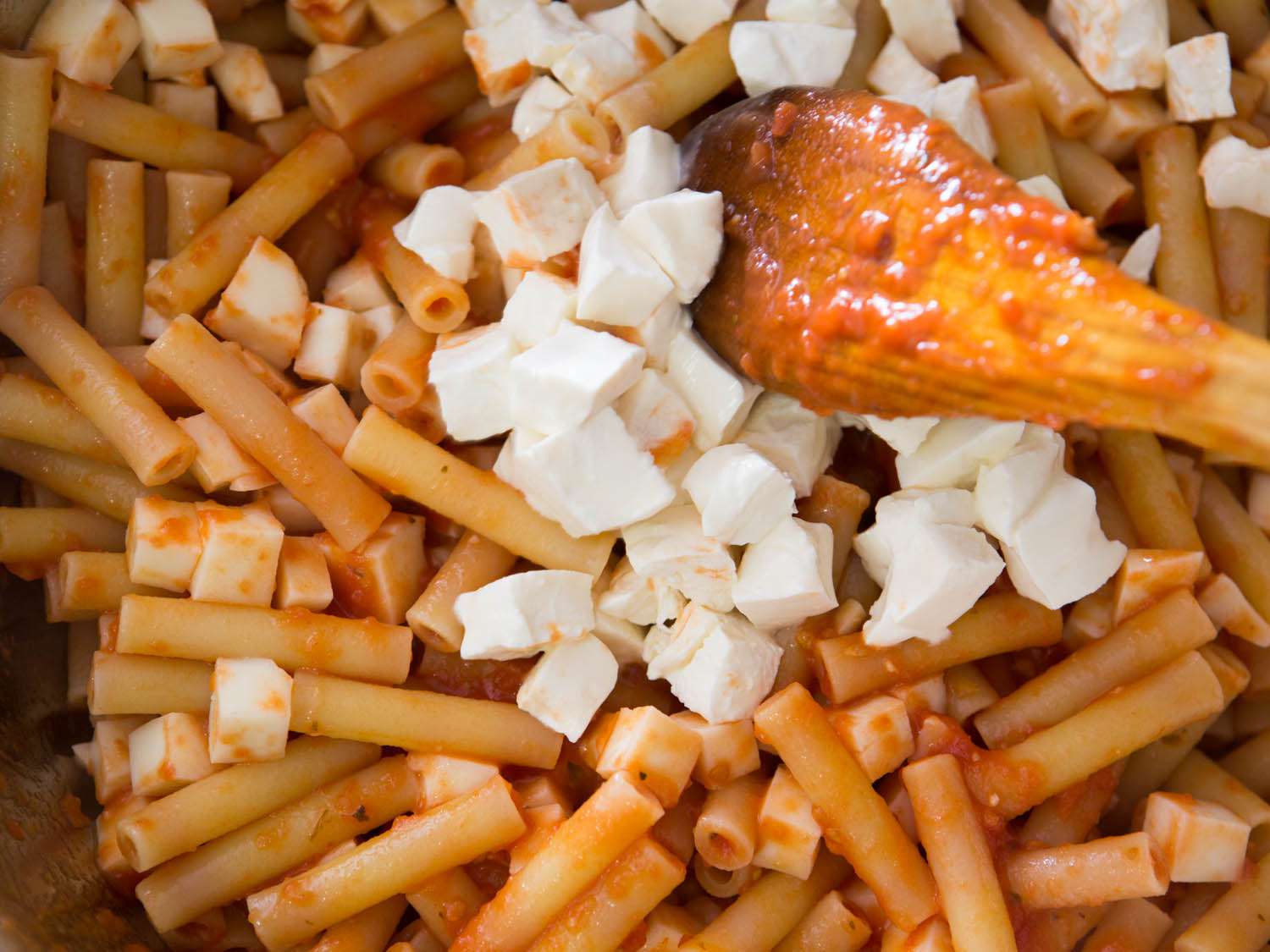 Cubed fresh mozzarella being tossed in ziti and tomato sauce.
