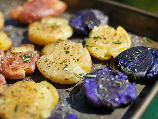 Smashed red, yellow, and purple potatoes on a baking sheet with salt, black pepper, and rosemary.