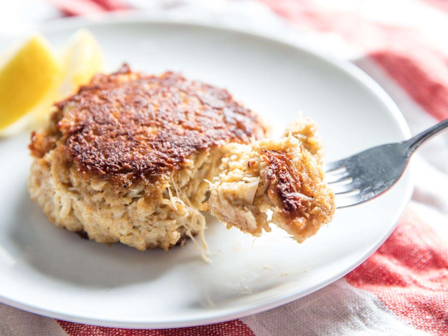 A forkful of golden brown Maryland crab cake is raised from the plate.