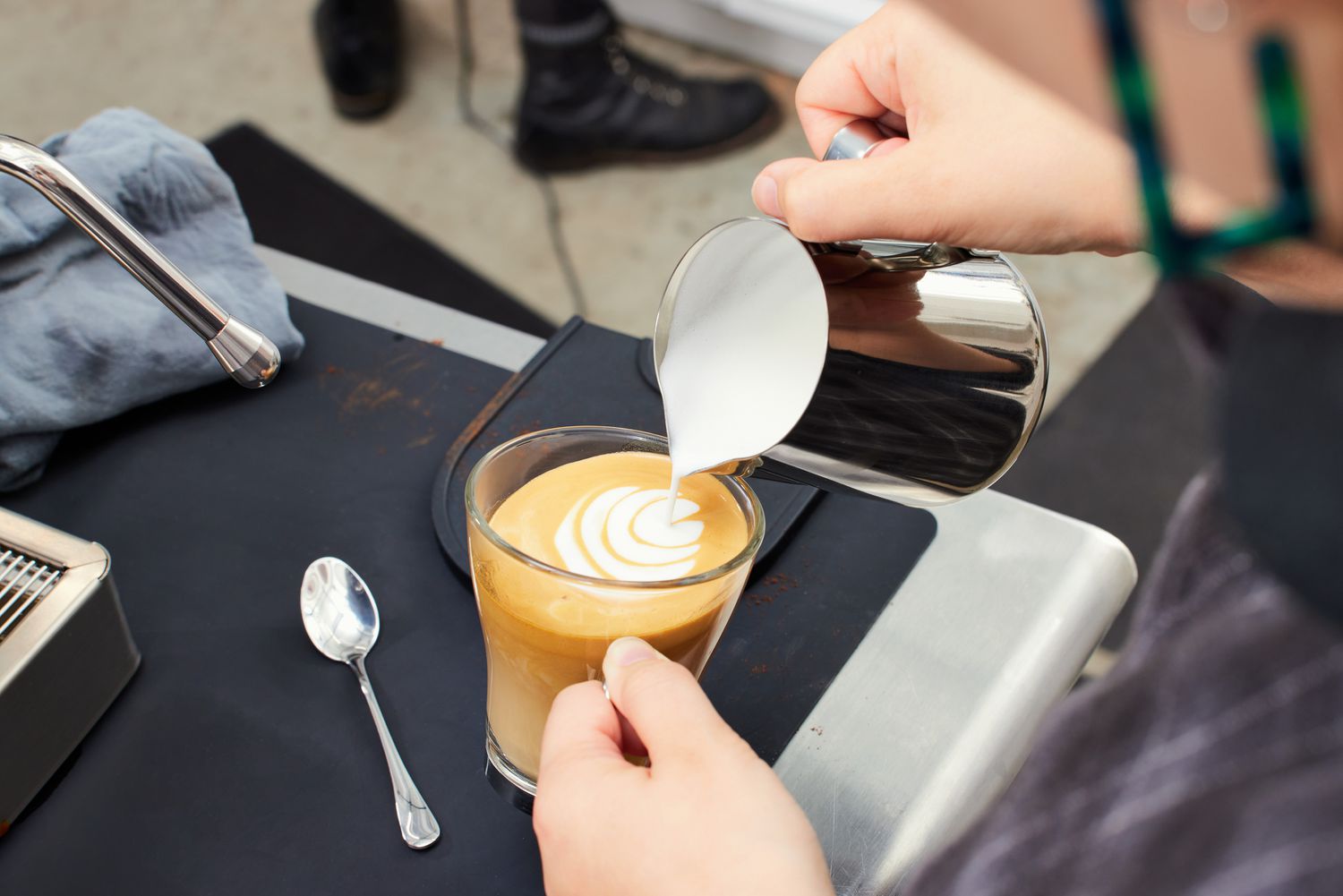 A person pouring milk into an espresso in a glass cup 