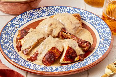 A plate of mole blanco sauce over chicken served on a decorative dish with accompanying dinnerware visible