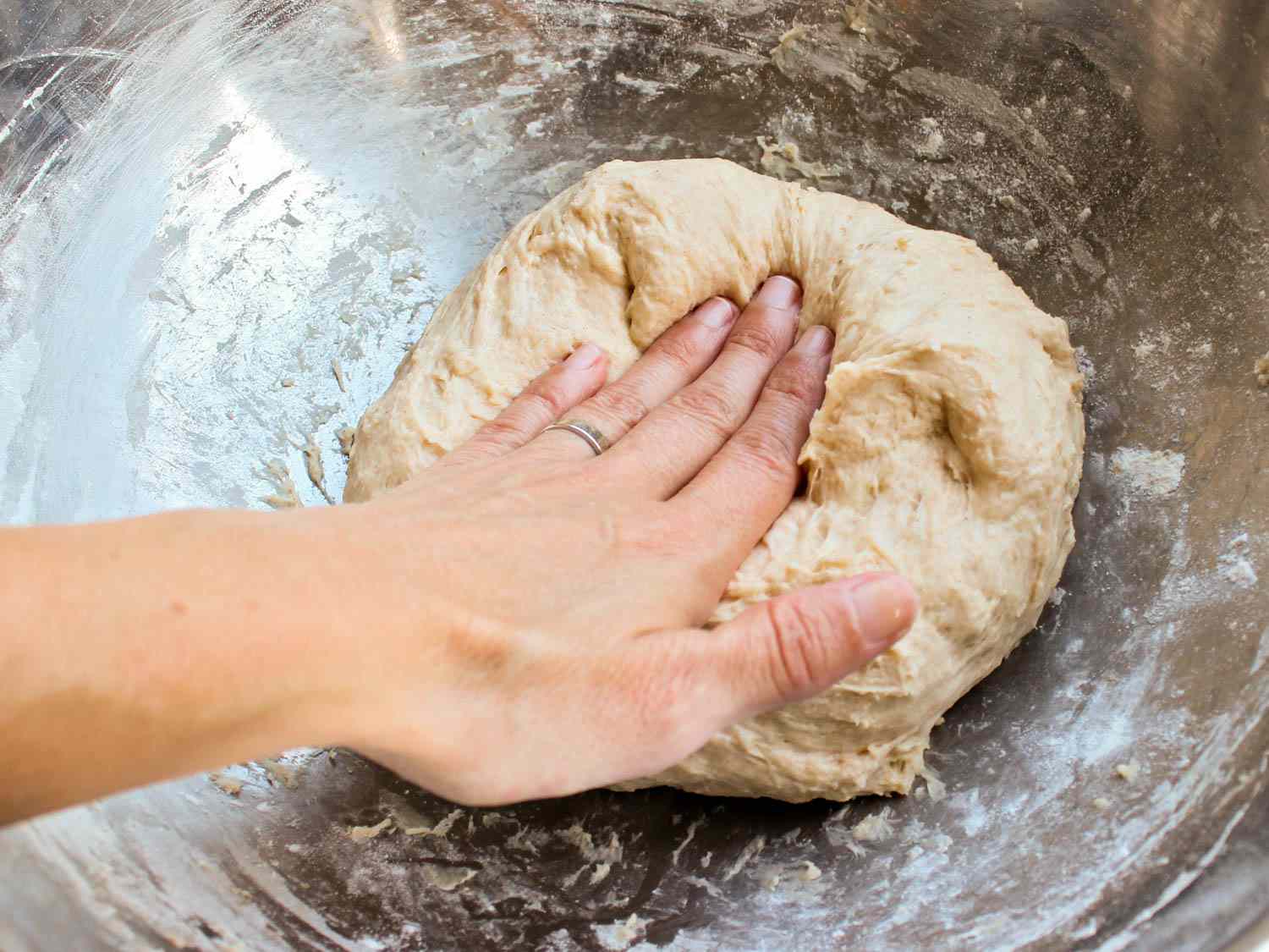 A hand kneading pita dough in a bowl.