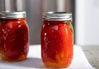 Two quart jars of canned tomatoes placed on a paper towel, gleam in the sunlight.