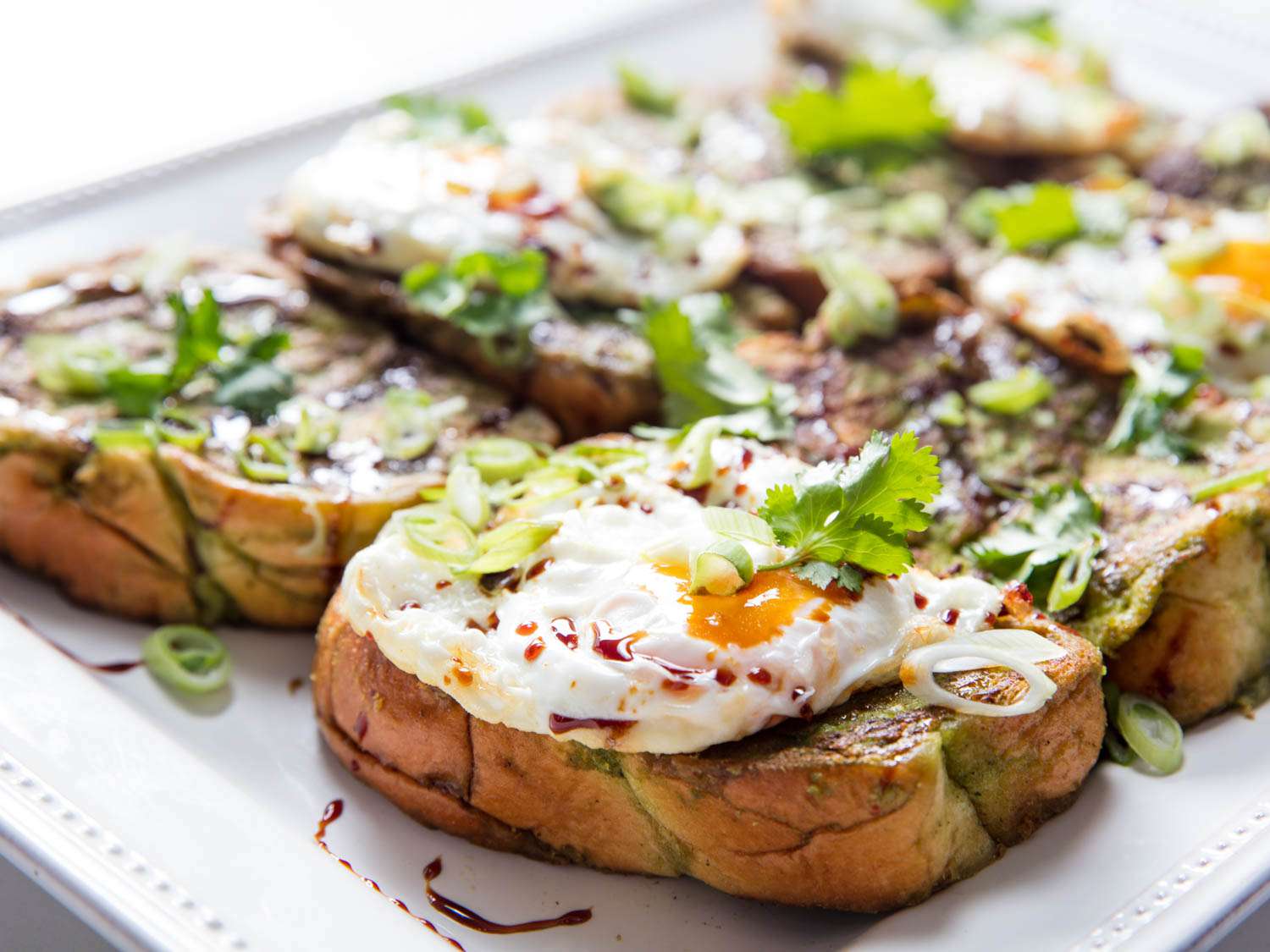 Side view of savory green curry French toast topped with poached egg and herbs.
